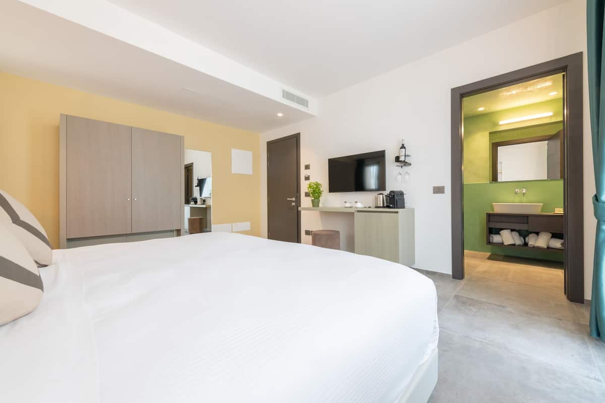 Ein Hotelzimmer mit Bett, Kleiderschrank, Fernseher und Badezimmer mit Waschbecken und Spiegel.
