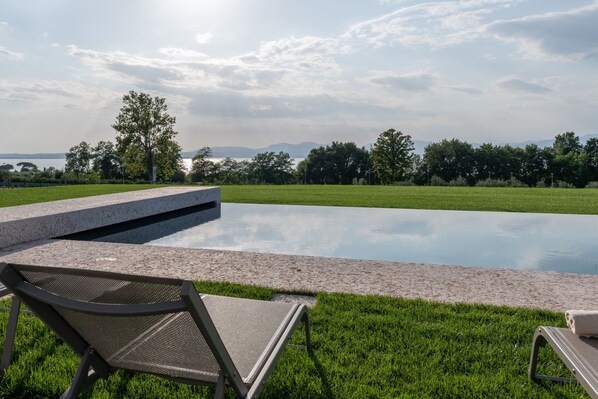 Piscina con dos sillones de descanso, rodeada de césped y árboles, con vistas a montañas distantes.