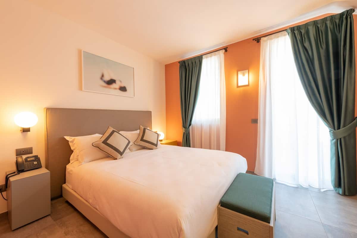 Ein Hotelzimmer mit Bett, Nachttisch, Lampe und Vorhängen.