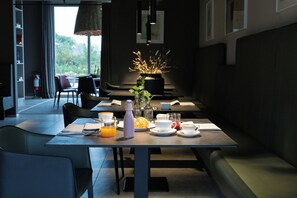 Un comedor moderno con una mesa dispuesta para el desayuno, que incluye una botella de jugo de naranja, un croissant y un jarrón con plantas secas.
