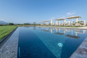 A clear blue pool with lounge chairs and umbrellas, surrounded by greenery and a clear sky. - Natiia Relais - Adults Only (Lazise)