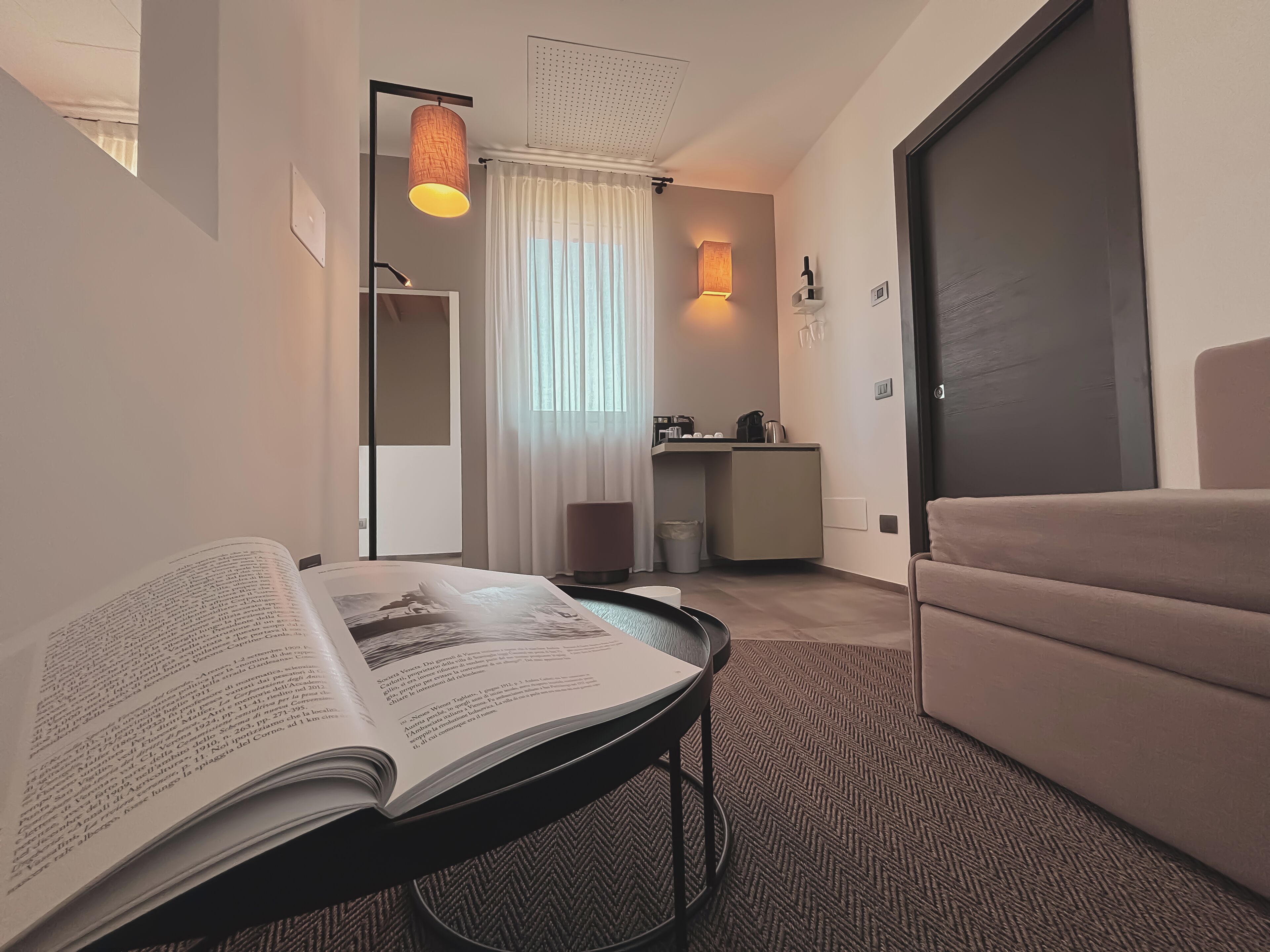 Ein modernes Hotelzimmer mit einem großen Bett, einer Leseecke mit einem Buch, einem kleinen Tisch und einer Küchenzeile.