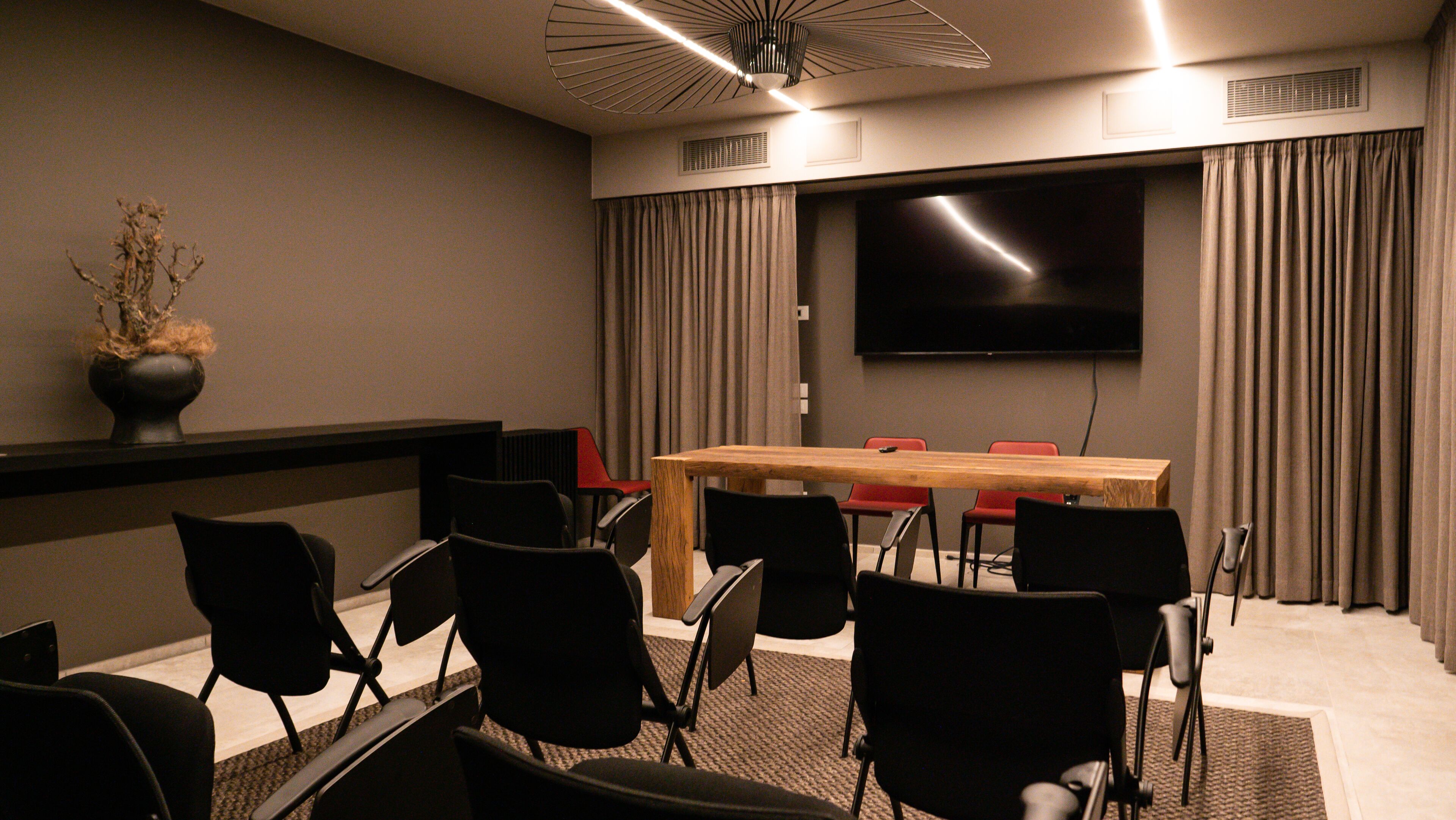 Une salle de conférence équipée d’un grand téléviseur à écran plat, d’une table en bois et de plusieurs chaises noires.