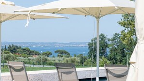 Sillas de descanso al aire libre con sombrillas, zona ajardinada y vistas al mar y al paisaje distante.