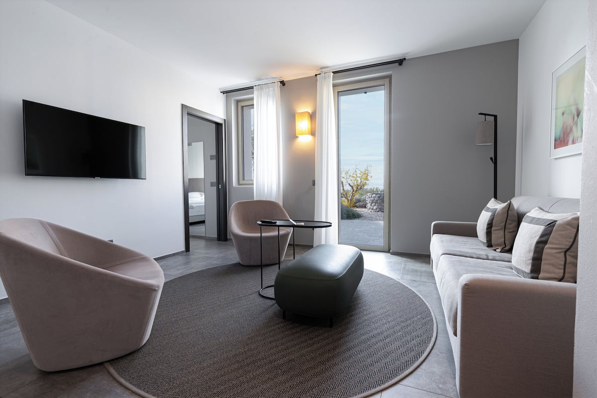 Ein modernes Wohnzimmer mit Flachbildfernseher, einer Couch, einem Sessel und einem kleinen Tisch.
