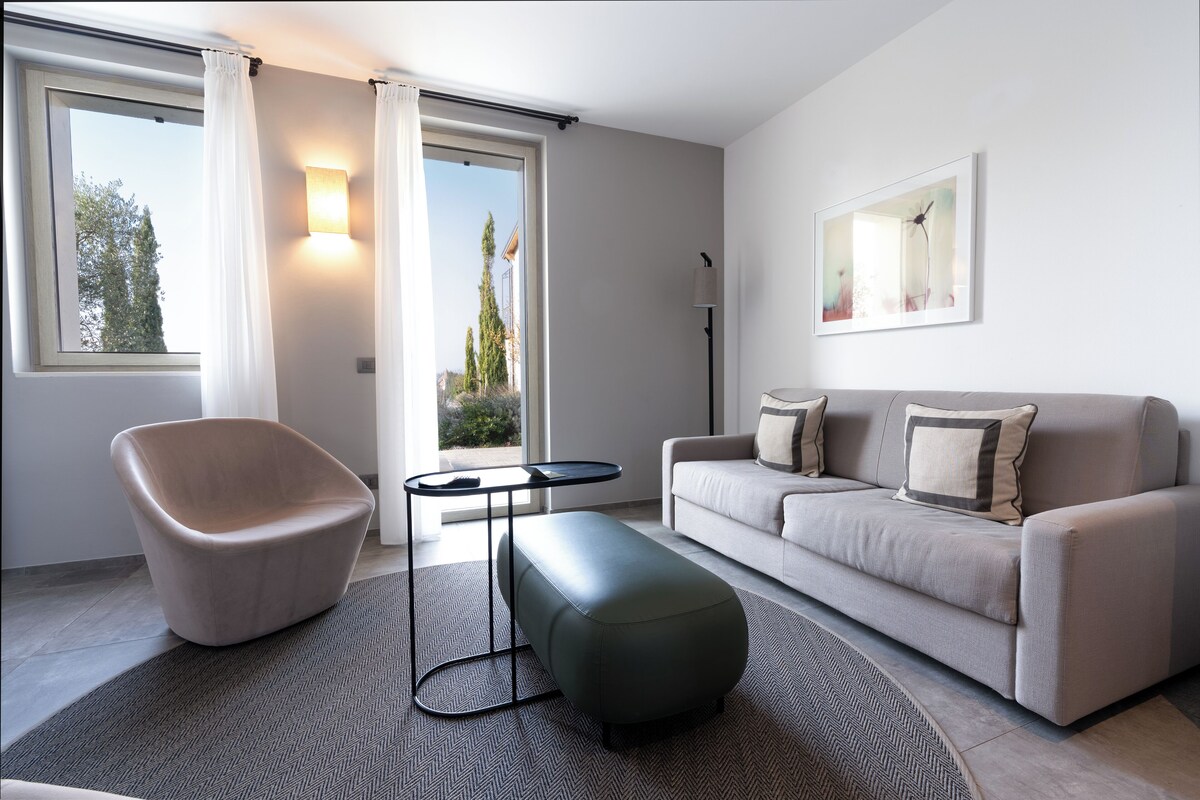 Una sala de estar moderna con un sofá, un sillón, una mesa de centro y un gran ventanal con cortinas.