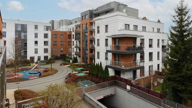 Un moderno complejo de apartamentos con varios edificios, un parque infantil y una pequeña piscina.