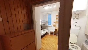 A room with a wooden dresser, a bunk bed, a small table, and a toilet.