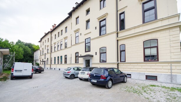 A building with multiple windows and a parking area with several cars.