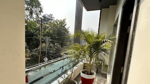 Varanda com vasos de plantas, guarda-corpo de vidro e vista para árvores e edifícios.