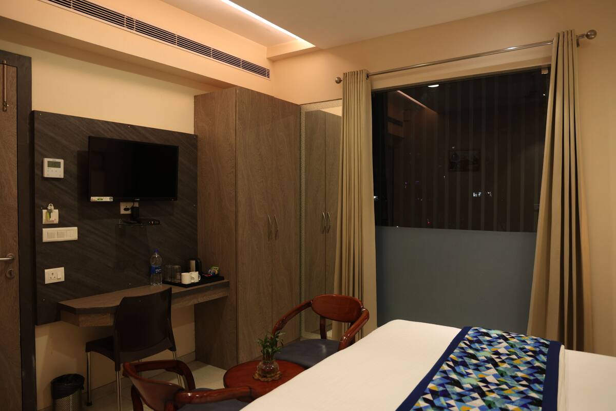 A hotel room with a bed, a desk, a chair, a TV, and a window with curtains.