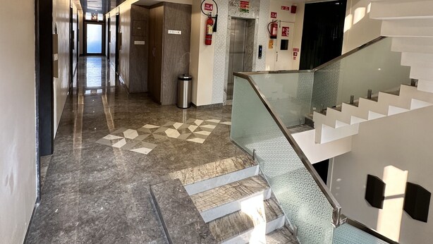 Um saguão de hotel moderno com piso de mármore, escada de vidro e vista para o mar.