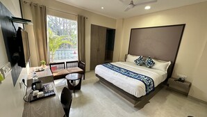 Quarto de hotel moderno com cama, escrivaninha, cadeira e vista para o verde lá fora.