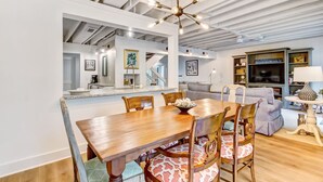 Un comedor con una mesa y sillas de madera, una cocina al fondo y una sala de estar con sofá y televisor.