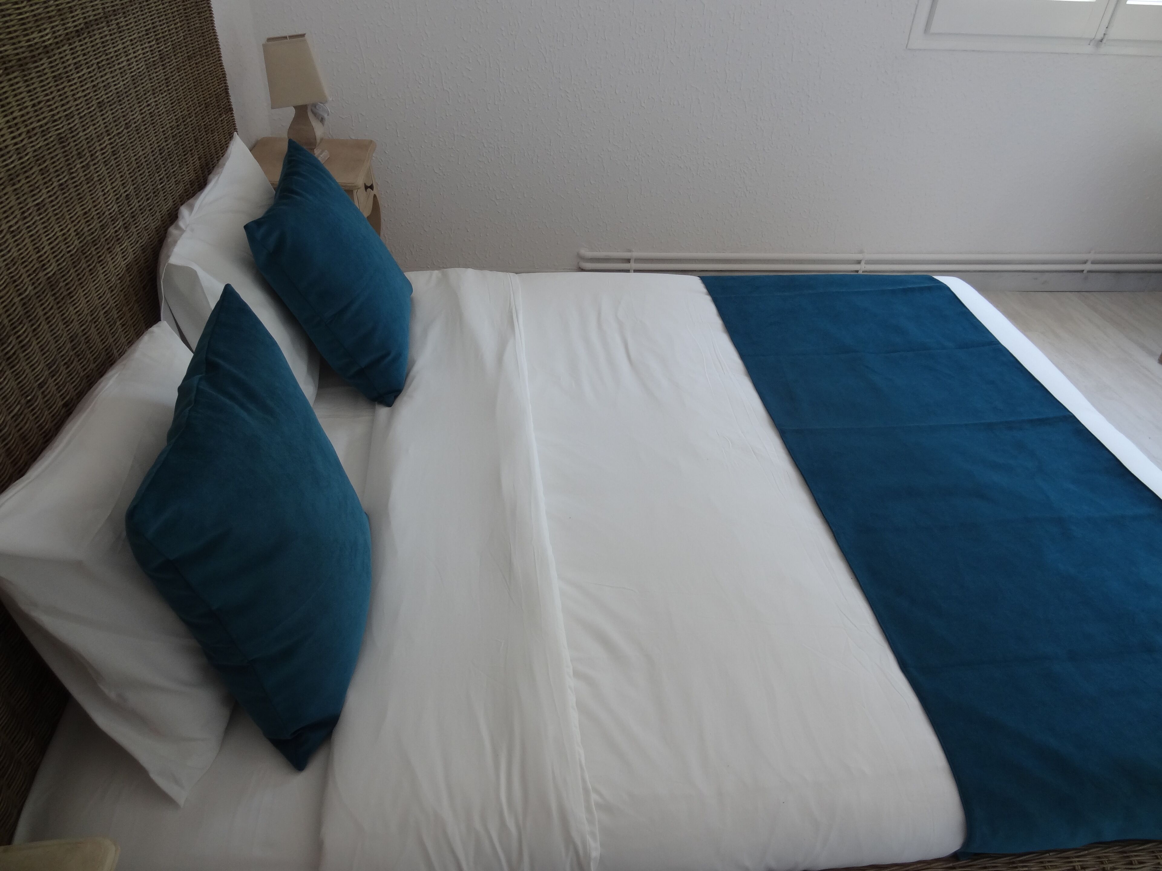 Una cama bien hecha con ropa de cama blanca y azul, un cabecero de madera y una mesita de noche con una lámpara.