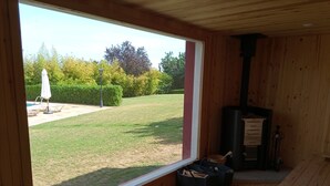 Una habitación de madera con un ventanal grande, chimenea y un pequeño espacio al aire libre con césped y árboles.