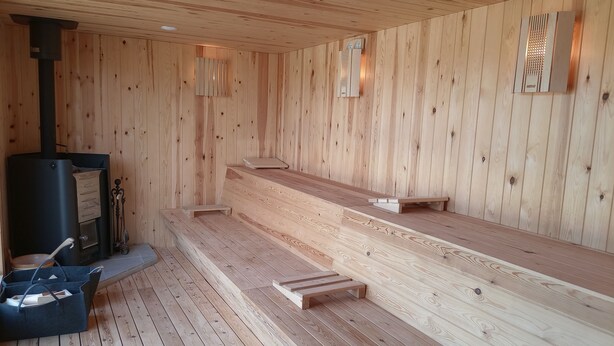 Un sauna con paredes y bancos de madera, un calentador de sauna y una pequeña mesa con un bolso.