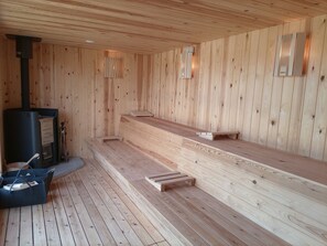 A sauna room with wooden walls and benches, a sauna unit, and a small table with a bag. - Private Tennis-Voleyball-Basketball, Heated Pool, Sauna with Aromatherapy (El Corral d'en Tort)