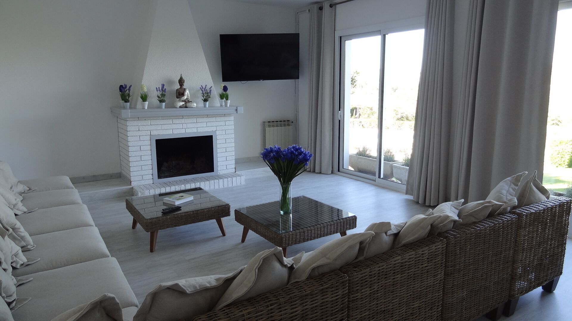 A living room with a white fireplace, a flat-screen TV, a sofa, a coffee table, and a wicker chair.