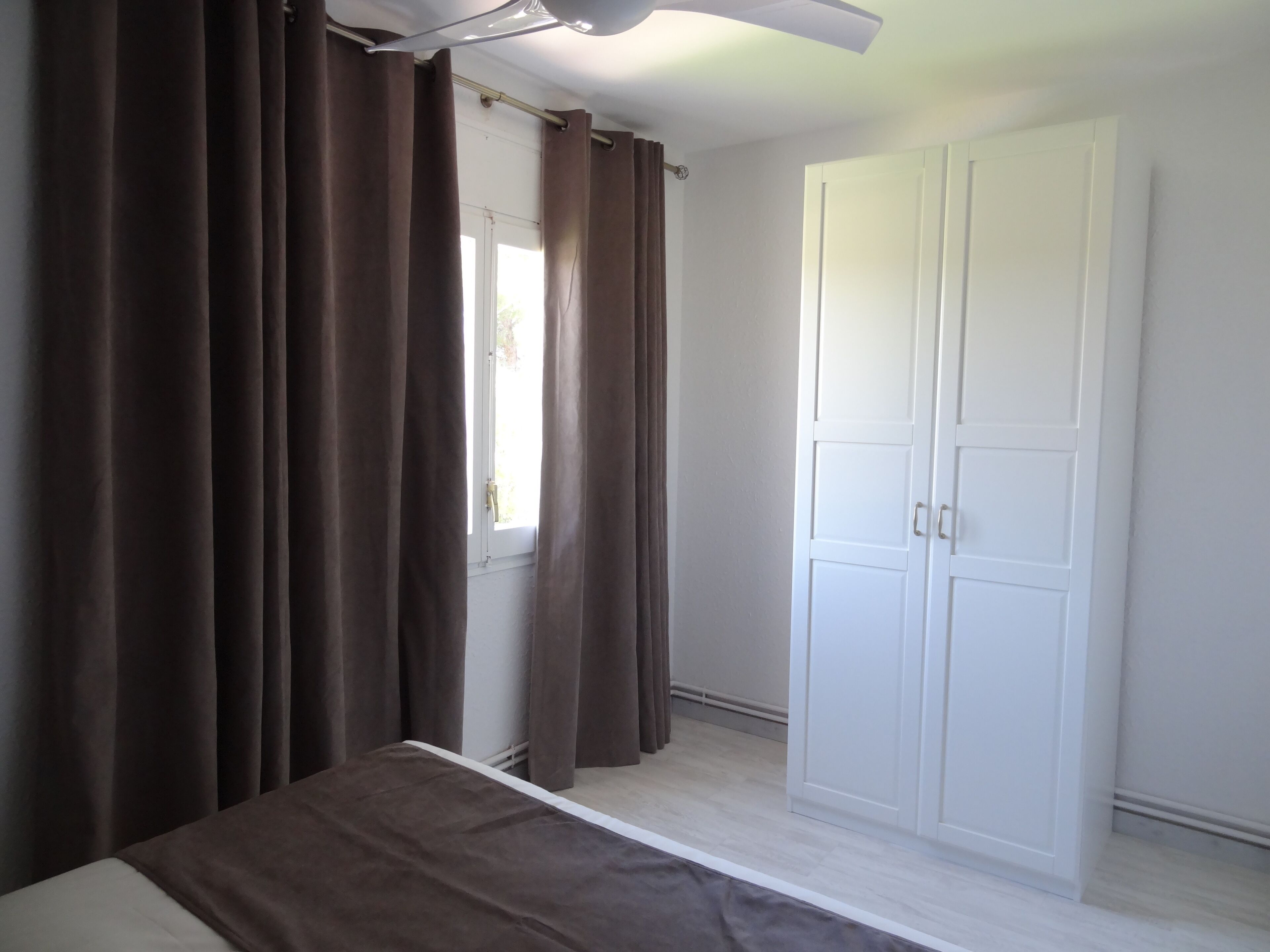 Ein Schlafzimmer mit einem Bett, einem Kleiderschrank und einem Fenster mit Vorhängen.