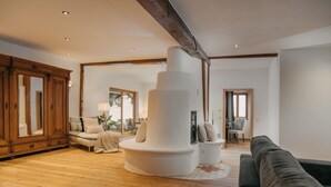 A spacious living room with a wooden floor, a large white pillar, a dark green sofa, and a wooden cabinet. - Apartment with 180sqm - in a former quiet farmhouse (Weitnau)
