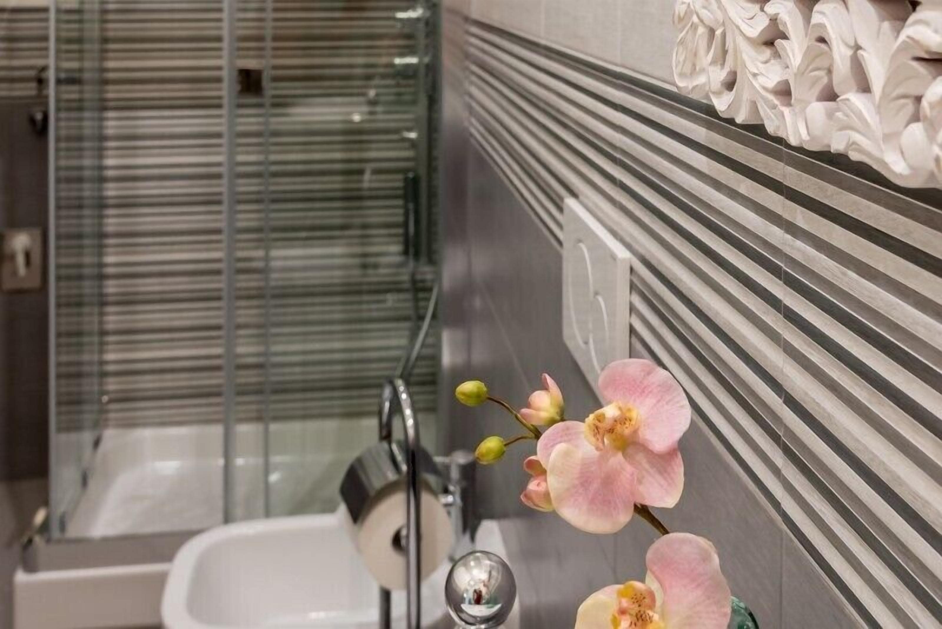 A bathroom with a glass shower enclosure, a white bathtub, and a decorative orchid arrangement on the wall.
