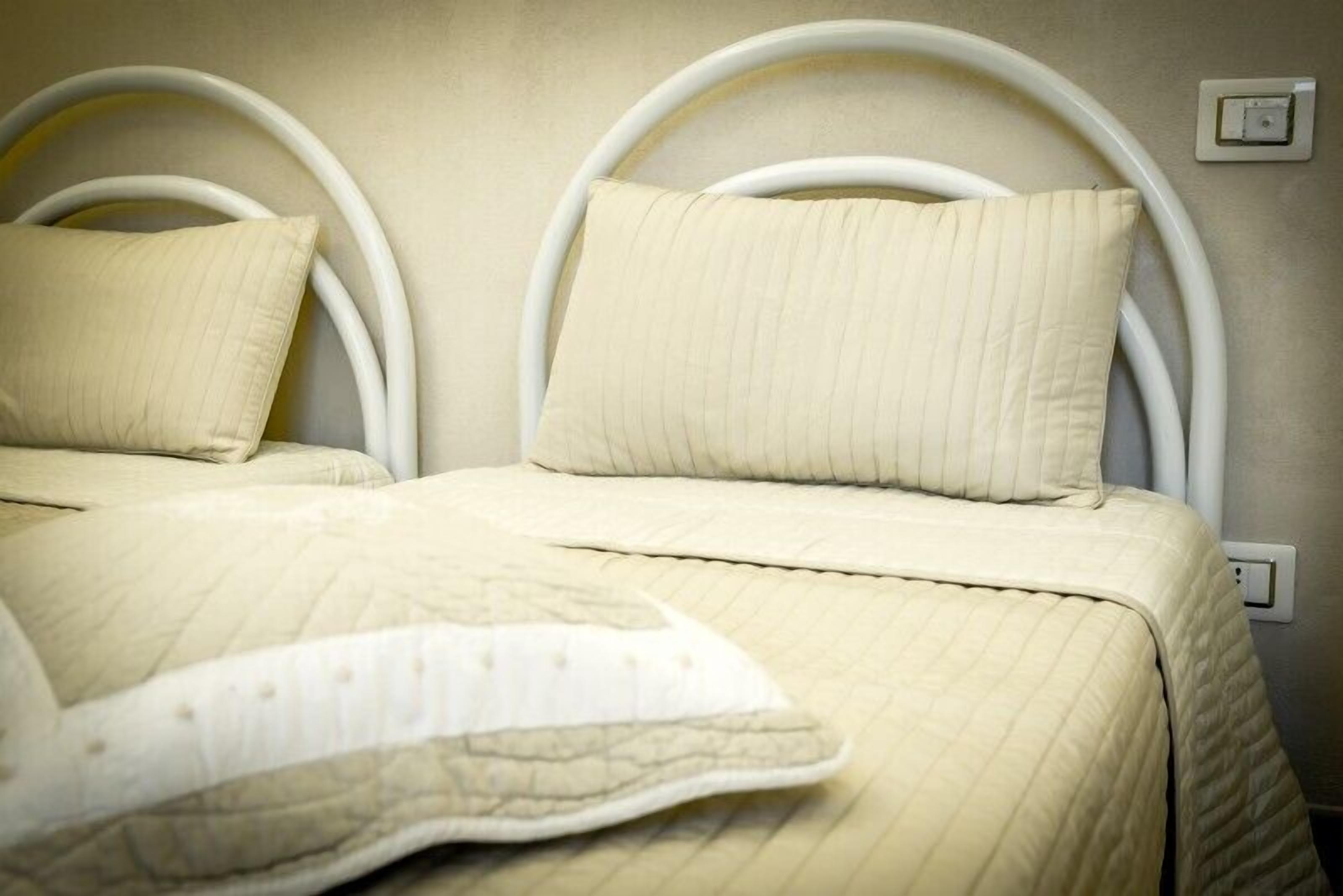 Dos camas con cabeceros blancos y ropa de cama color crema.