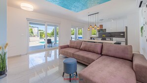 Un salon moderne avec un grand canapé d’angle, un petit pouf et un plafond orné d’un motif texturé bleu.