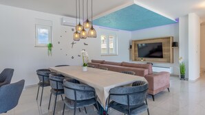 Un salon moderne doté d’un grand téléviseur, d’une table à manger avec des chaises, d’un canapé et d’un plafond agrémenté d’une touche de couleur bleue.