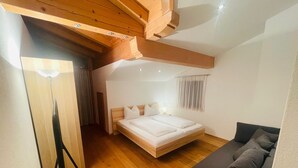 Et soveværelse med træloft, en seng med hvide sengetøj, en grå sofa og en gulvlampe.