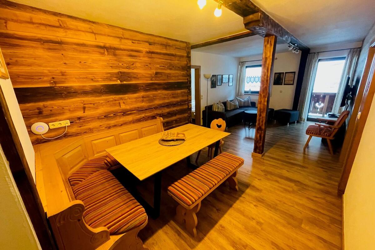 A cozy interior with a wooden wall, a dining table with benches, and a sofa in the background.