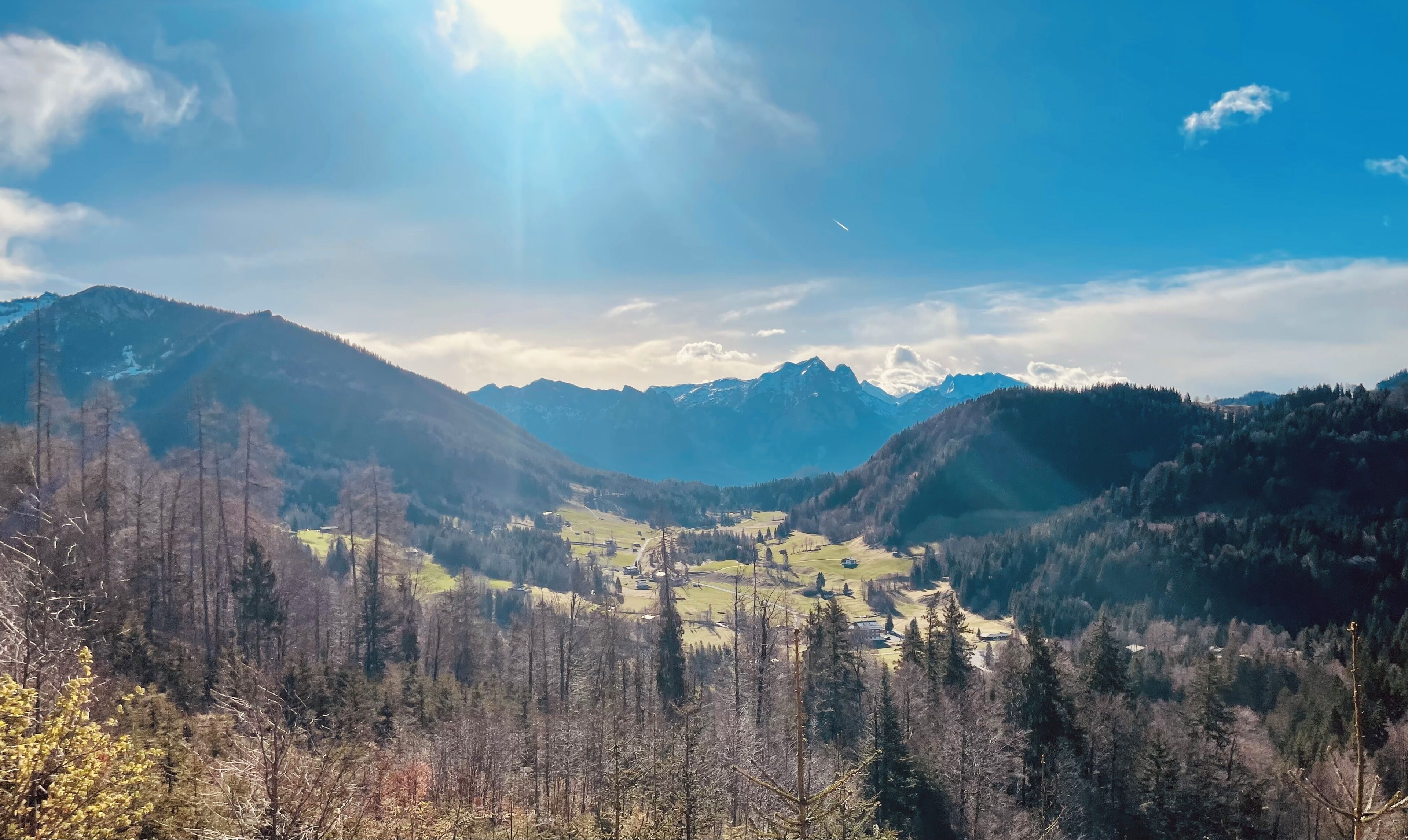 Eine gebirgige Landschaft mit einem Tal, Bäumen und einer kleinen Siedlung.