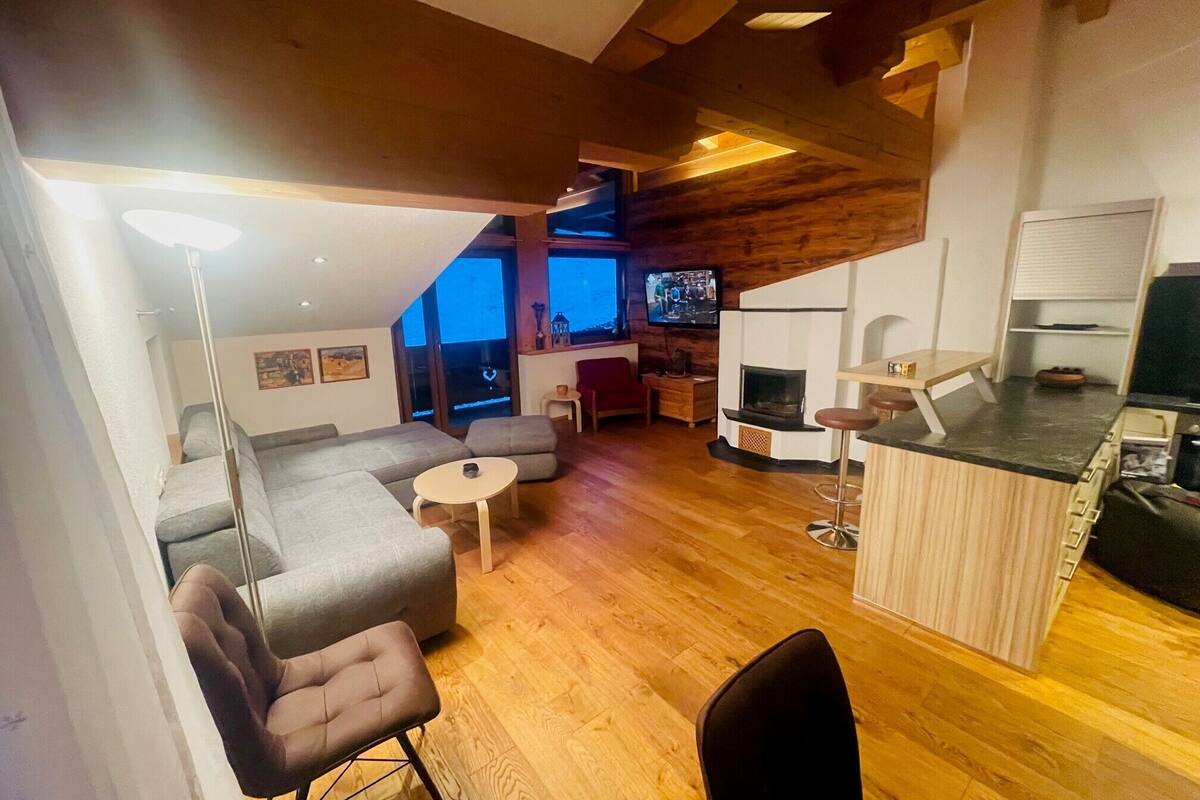 A modern living room with a sofa, chairs, a small round table, and a TV.