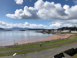 A coastal view with a beach, a calm sea, and a town in the background.