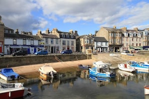 A harbor with boats docked, a sandy breakwater, and buildings with shops and restaurants.
