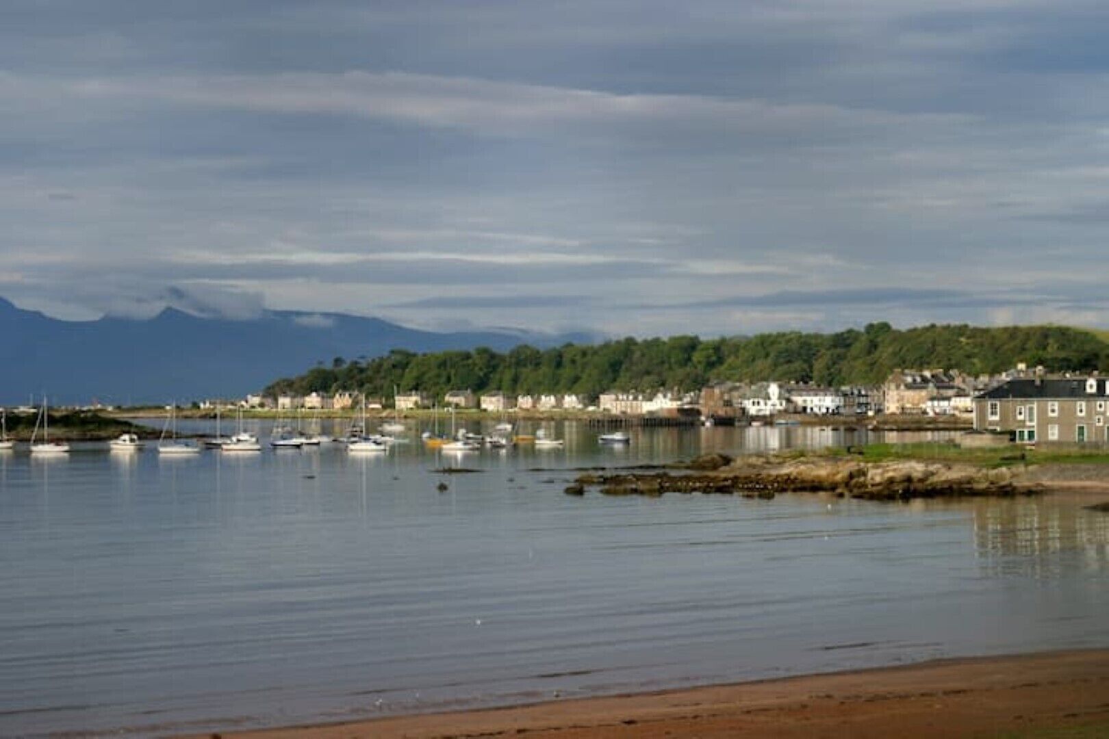 A coastal town with calm waters, boats, and buildings along the shore.