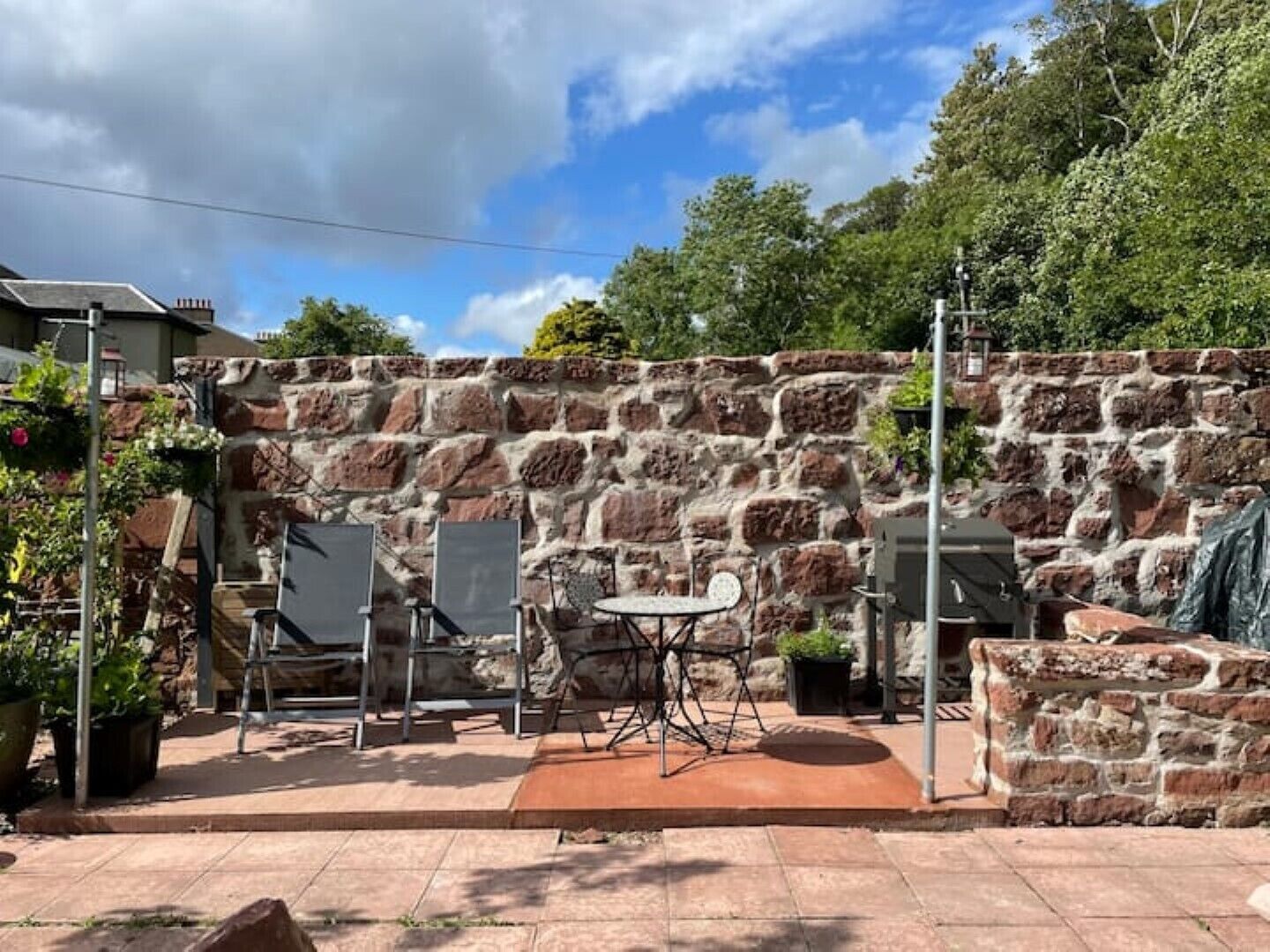 A patio area with a stone wall, a table with chairs, and potted plants.