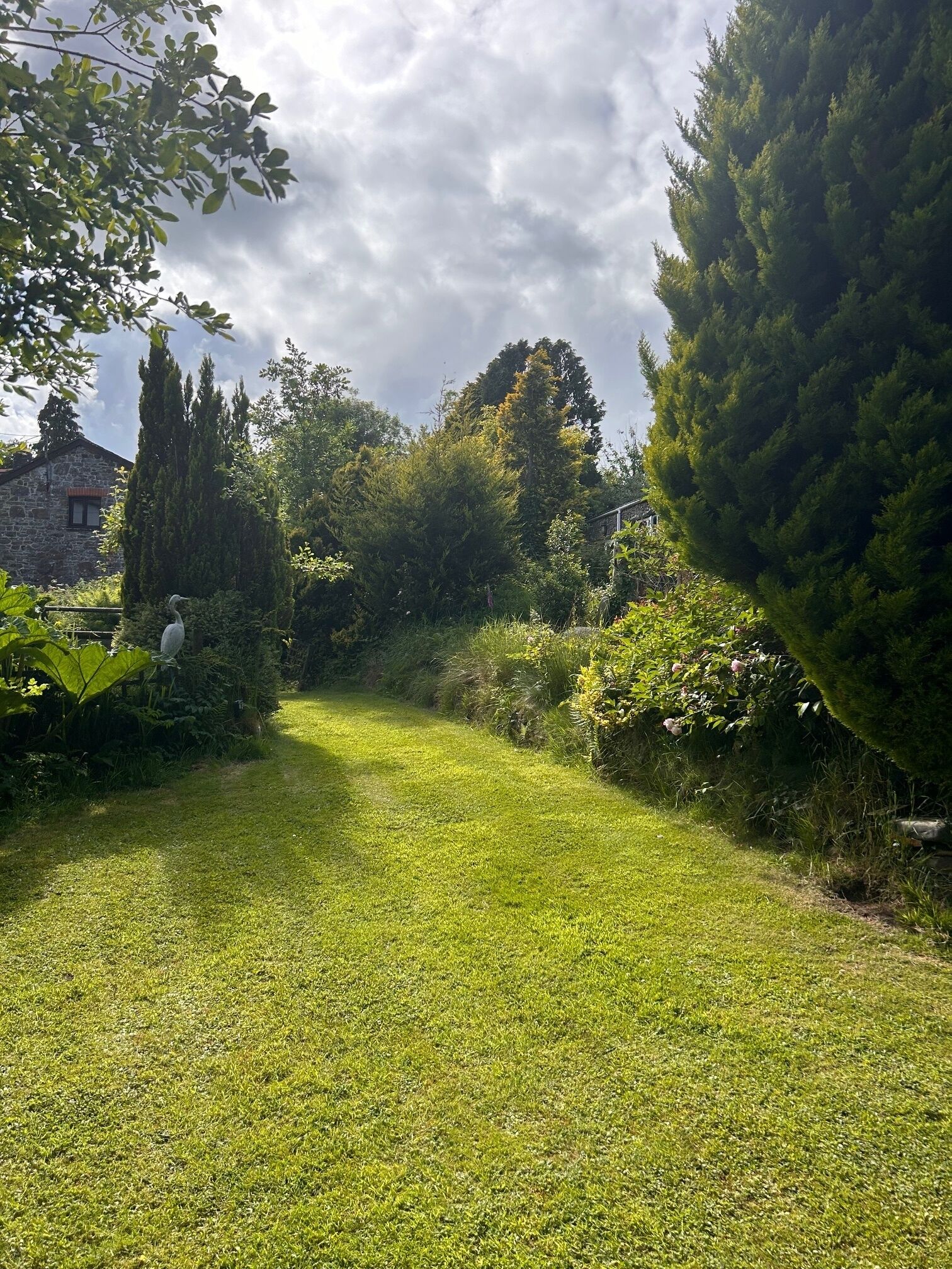A well-maintained grassy area with a variety of trees and shrubs, a stone building in the background, and a clear sky.