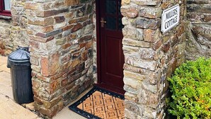 A stone cottage with a red door and a sign reading "Millers Cottage." - Millers cottage, a picturesque semi detached cottage with private garden (Woolfardisworthy)