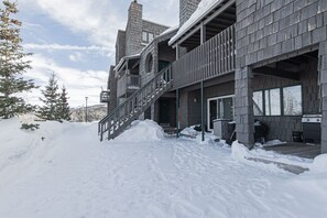 A two-story building with a wooden exterior, a staircase leading to the upper level, and a covered outdoor area with a grill.