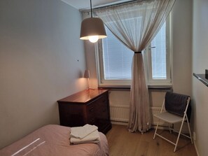 A bedroom with a bed, a wooden dresser, a chair, a window with blinds, and a hanging lamp. - Four rooms apartment close to the city center (Västra Götalands län)