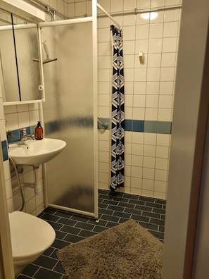 A bathroom with a white sink, a mirror, a shower with a patterned curtain, and a tiled floor. - Four rooms apartment close to the city center (Västra Götalands län)