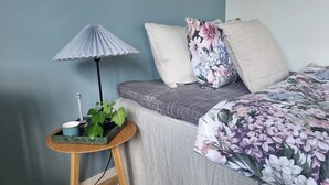 Ein Schlafzimmer mit einem Bett, einem Nachttisch mit Lampe und einer Pflanze.