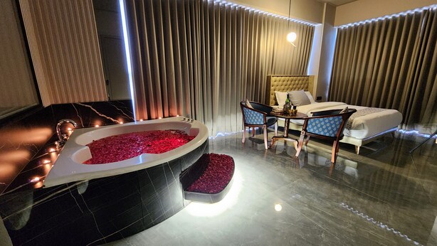 A modern bathroom with a large bathtub filled with rose petals, a separate shower area, and a seating area with a table and chairs. - Apricot Motera  (Ahmedabad)