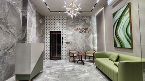 A lobby with marble walls, a modern chandelier, a green sofa, and a sign for 'A Price Hotel'. - Apricot Motera  (Ahmedabad)
