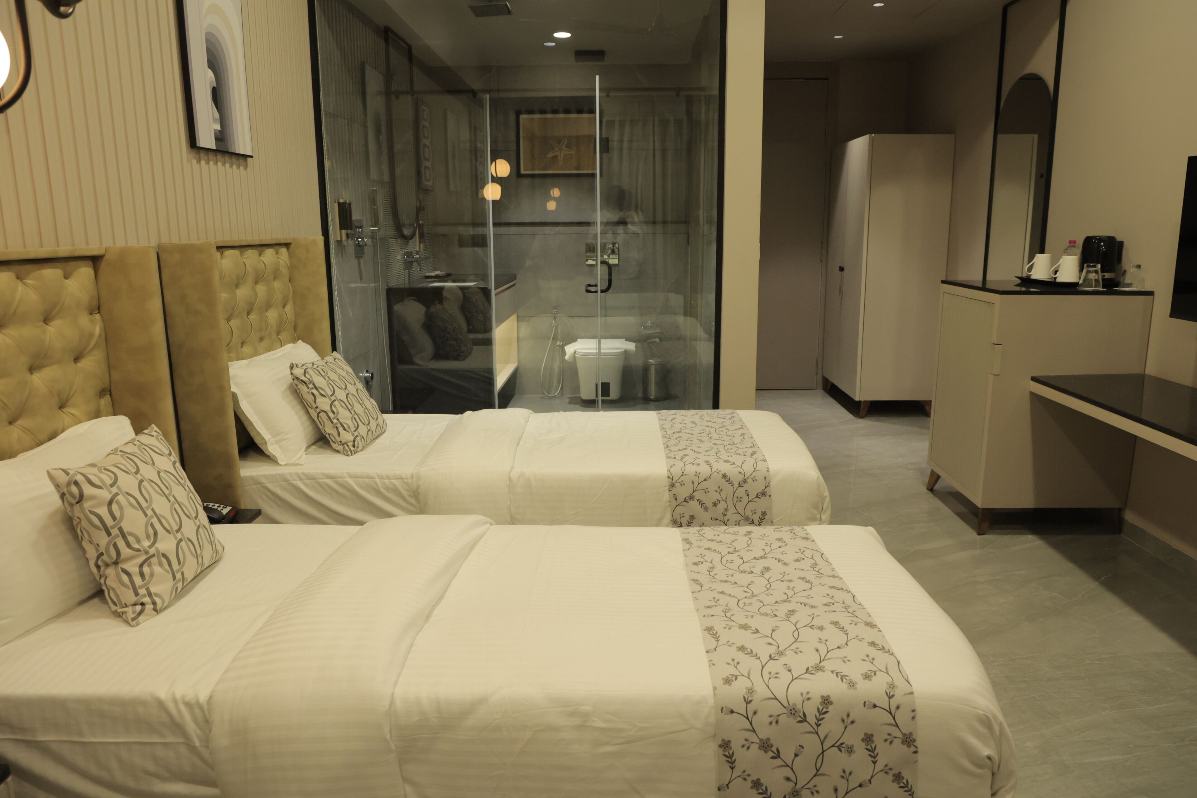 Habitación de hotel con dos camas, ducha envuelta en vidrio, minibar y televisión.