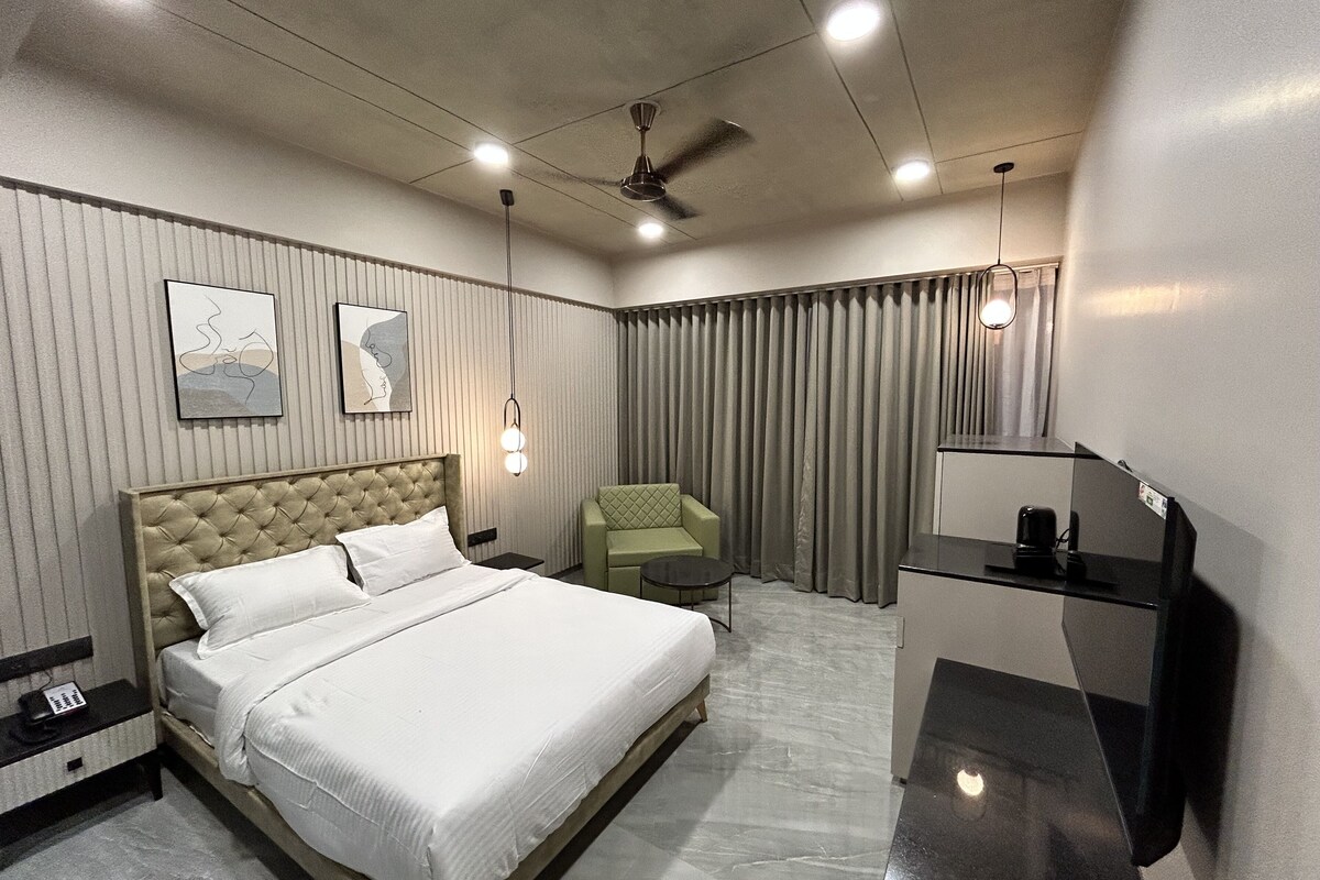 A modern hotel room with a large bed, a desk, a chair, a ceiling fan, and a TV.