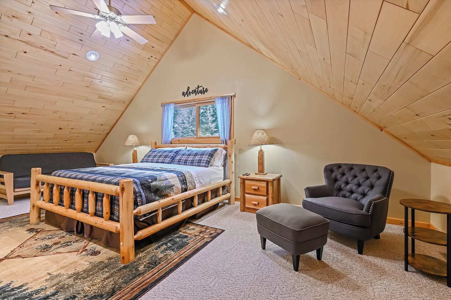 A cozy attic bedroom with a wooden ceiling, a bed with plaid bedding, a tufted armchair, and a small table.