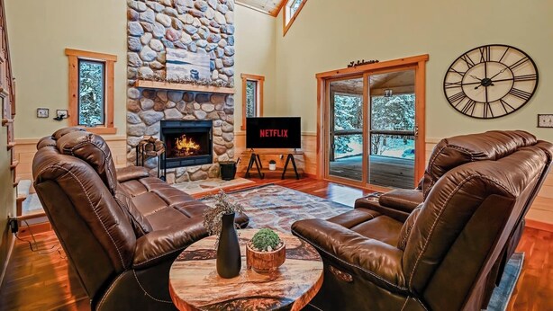 Una sala de estar acogedora con sofás de cuero, una chimenea de piedra, un televisor grande y un reloj en la pared.
