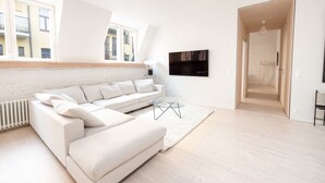 A modern living room with a white sectional sofa, a glass coffee table, and a view of a cityscape through large windows. - 2ndhomes Luminous 2BR Loft House w Sauna (Helsinki)